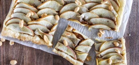 a sliced apple tart sitting on top of a wooden table.
