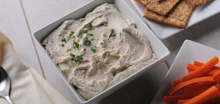 a bowl of hummus with carrots and crackers.