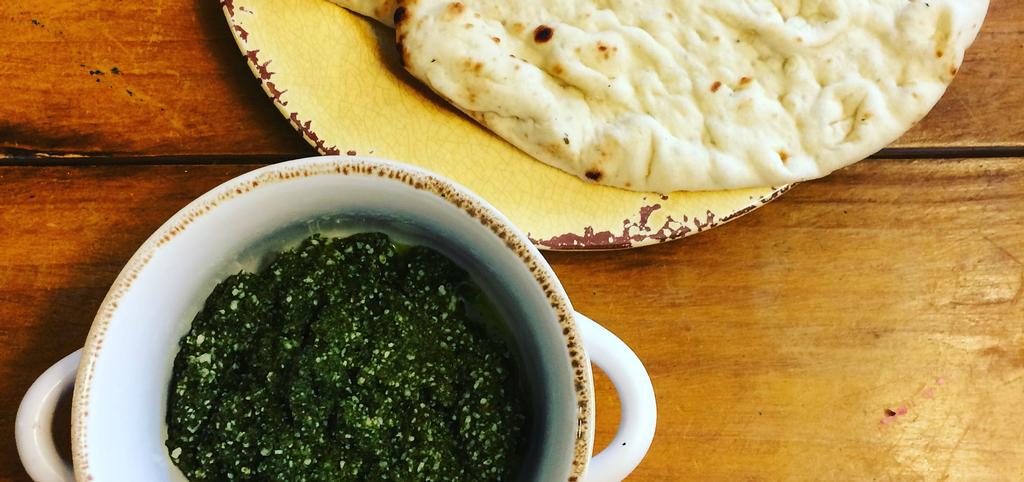 a bowl of pesto next to a plate of pita bread.
