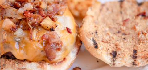 close up of a a open burger with chopped bacon on top.