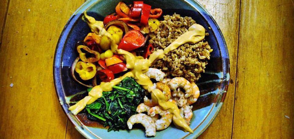 a bowl full of roasted vegetables and shrimp with peanut butter sauce crossed on top.