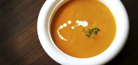 a bowl of soup decorated with a small herb and drips of white cream.