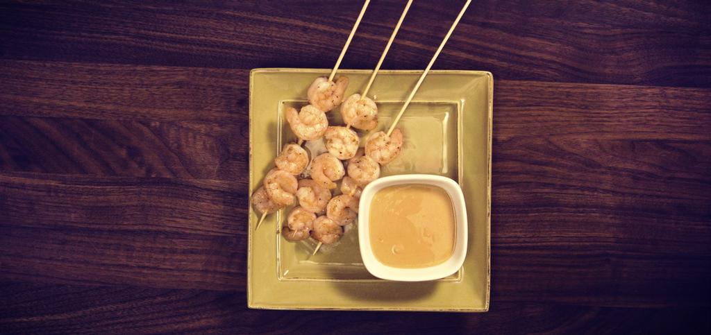 a plate topped with shrimp skewers and a dip sauce.