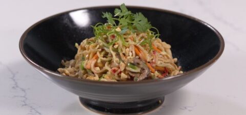 a noodle bowl mixed with vegetables and peanuts.
