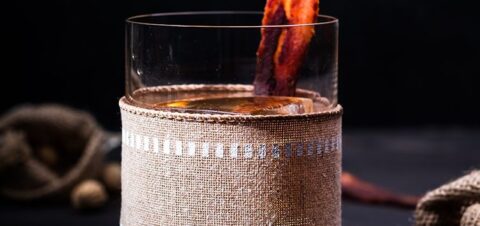 a cocktail drink garnished with a single slice of crispy bacon on top.
