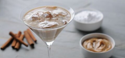 cocktail glass filled with a creamy drink next to peanut butter and cinnamon sticks.