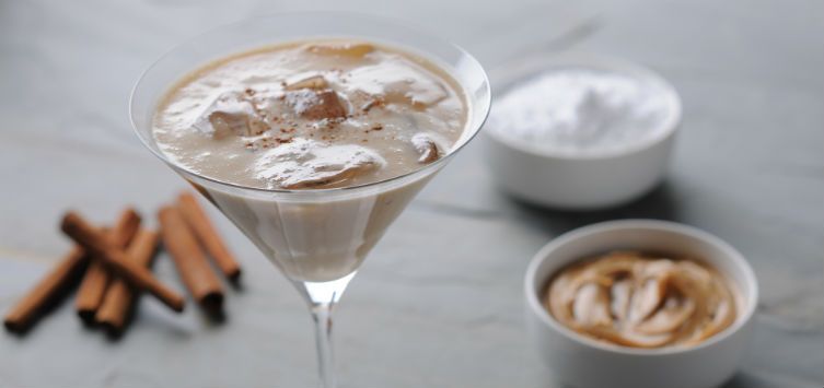 cocktail glass filled with a creamy drink next to peanut butter and cinnamon sticks.